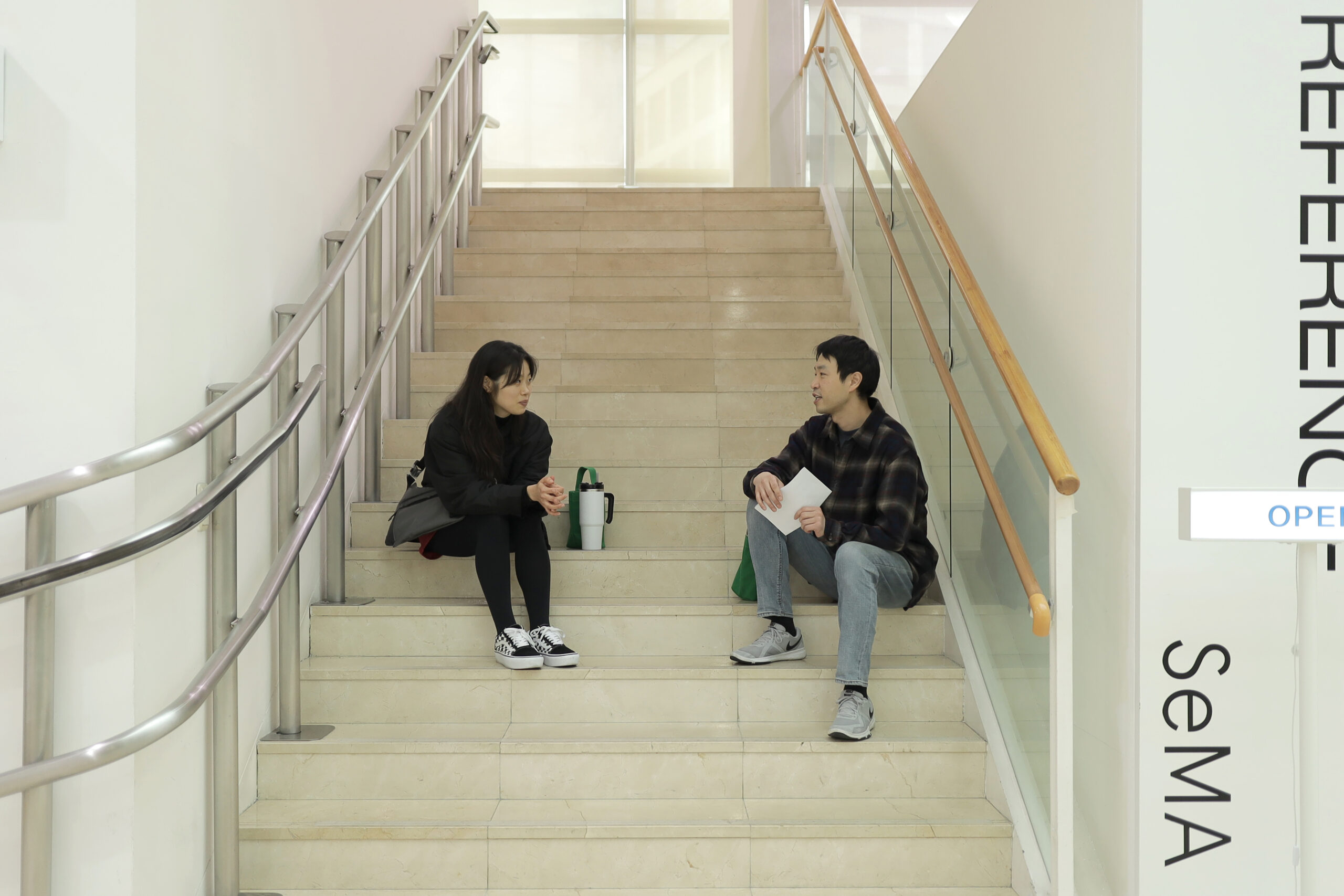 Two performers converse while sitting on the steps of a staircase.